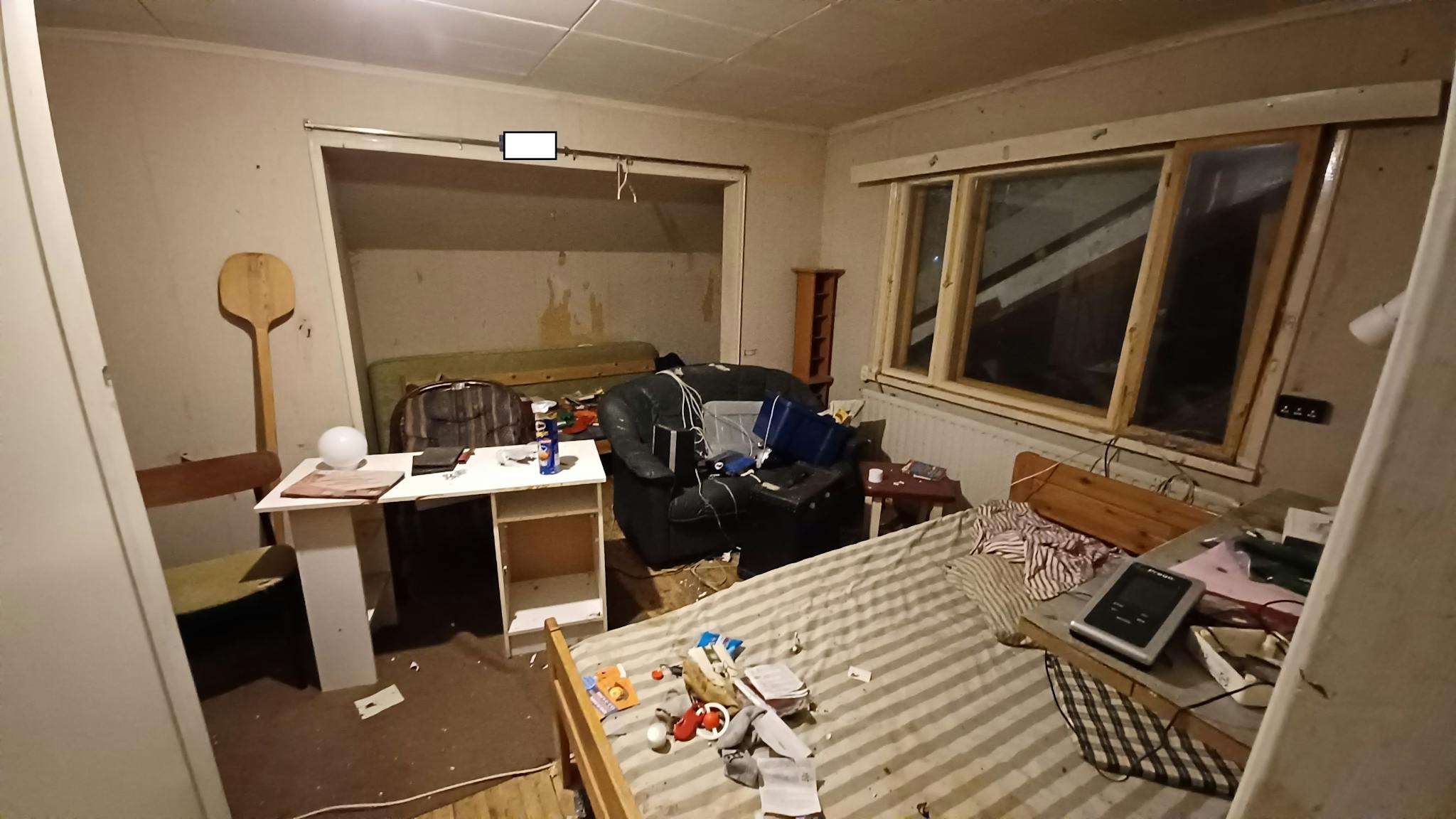 Asuinhuone, jossa on sänky ja pöytä. Ikkuna on oikealla seinustalla. Sen vasemmalla puoleisella seinustalla on syvennys.