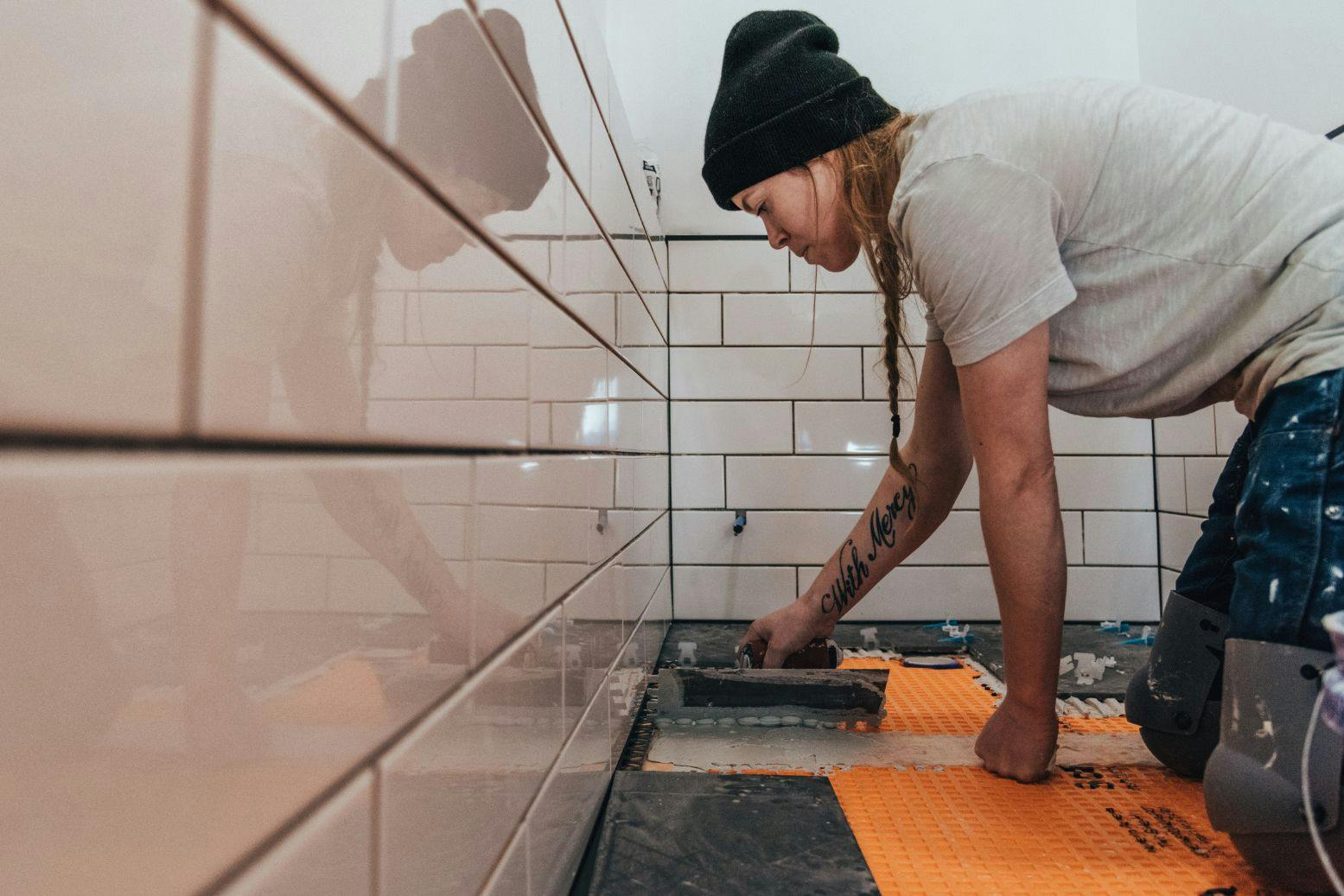 remonttialan ammattilaisnainen laatoittaa pipo päässä kylpyhuonetta polvillaan