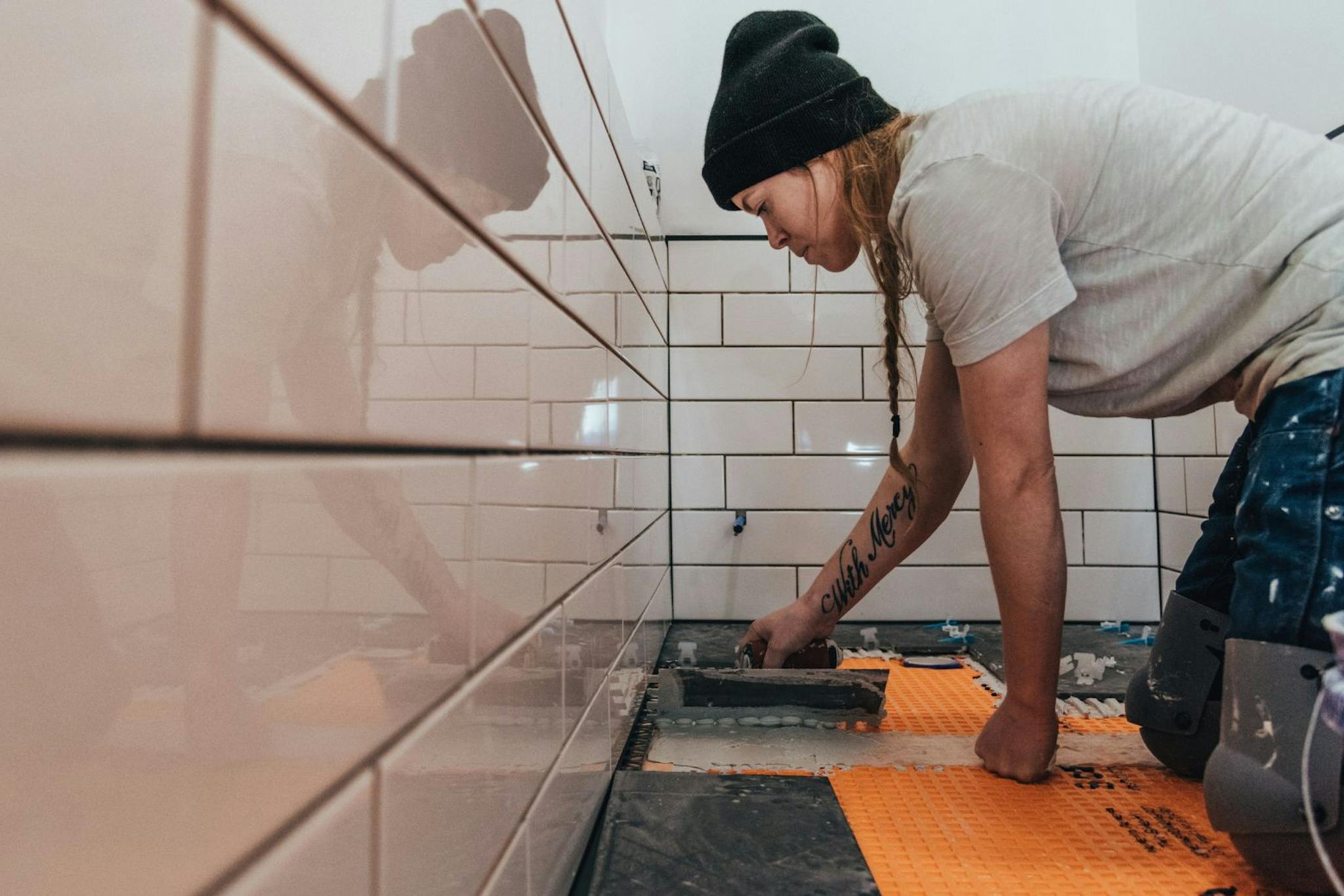 remonttialan ammattilaisnainen laatoittaa pipo päässä kylpyhuonetta polvillaan