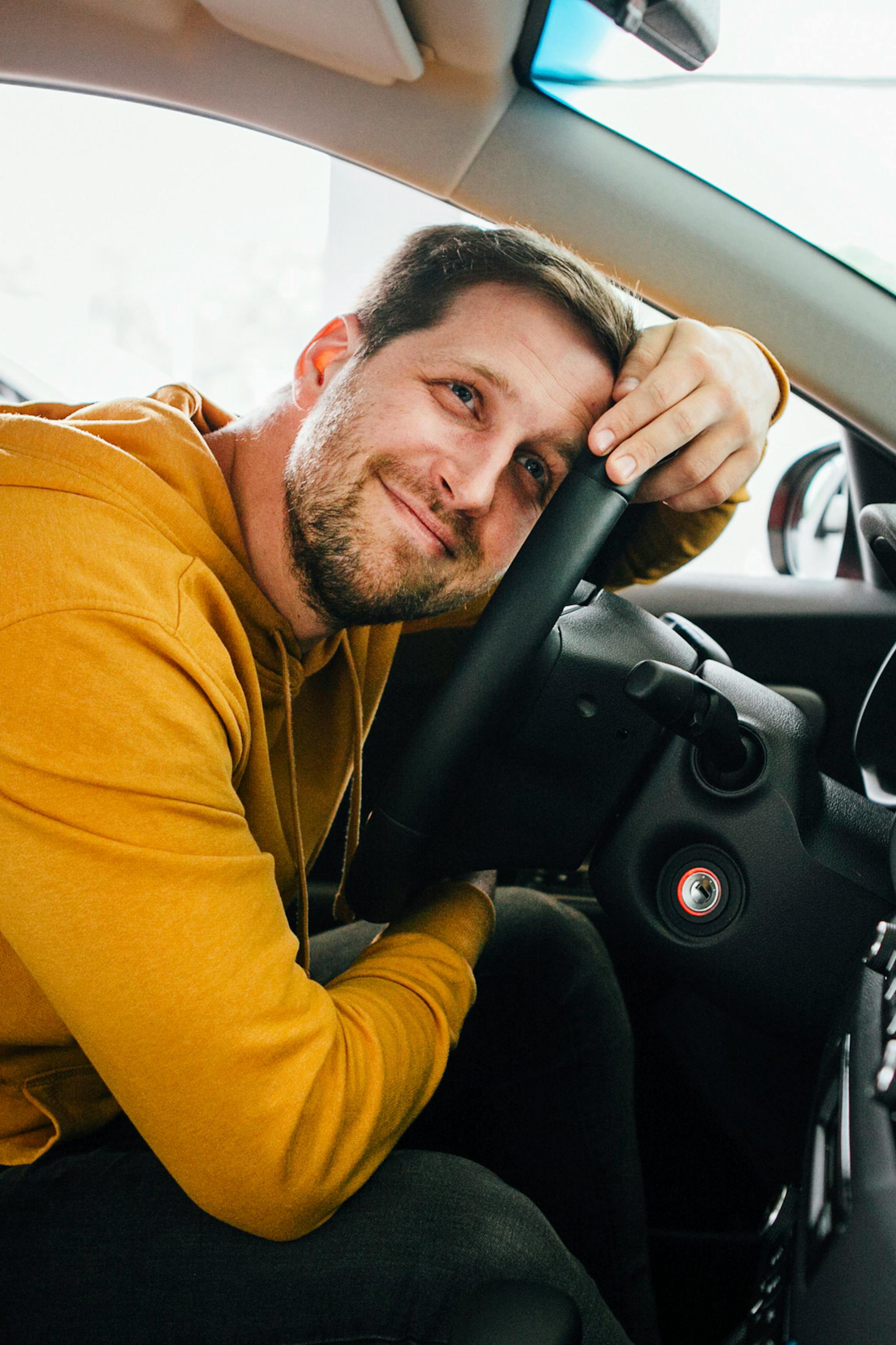 Mies hymyilee ja nojaa auton rattiin