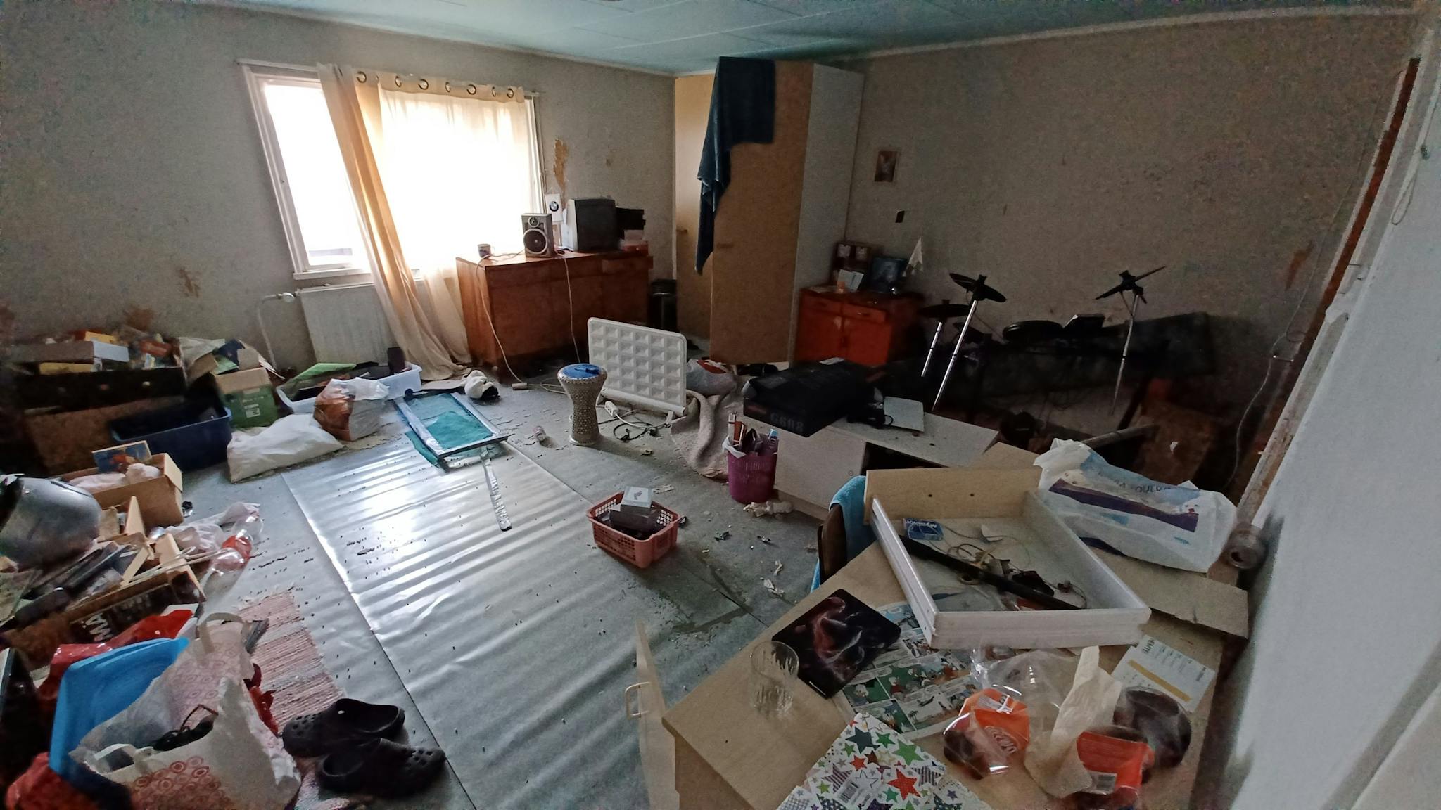 Asuinhuone, jossa on ikkuna ja korkeakaappi. Lattioilla on paljon sekalaista tavaraa.