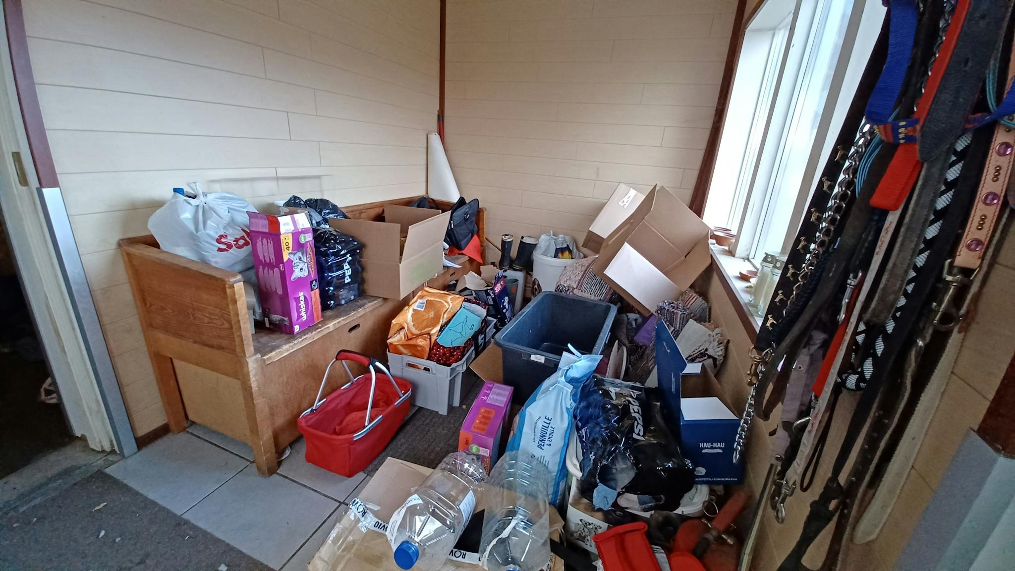 Eteinen, jossa on eläintenhoitoon liittyviä tarvikkeita. Laatta lattia ja vaaleat vaakapaneeliseinät.